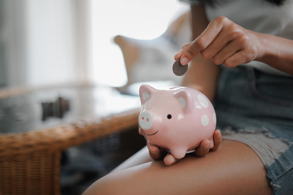 Menina colocando moedas dentro de um cofre em formato de porquinho.