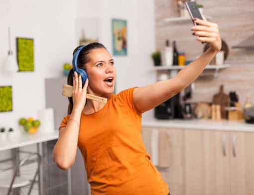 Mulher feliz, escutando música e tirando uma selfie, enquanto curte a própria casa.